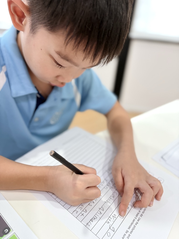 A child in a blue shirt writing on a sentence worksheet