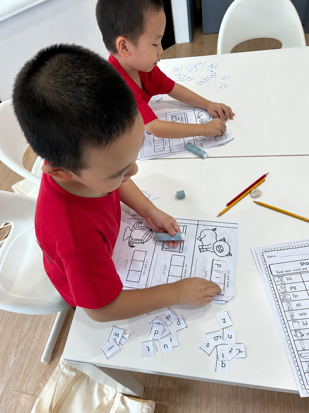 Two children arranging cut-out letters on word-building worksheets